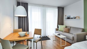 Una habitación de hotel moderna con una mesa de comedor de madera, dos sillas, un sofá, una mesita blanca y una cama.