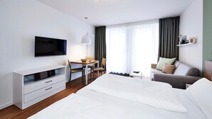 Una habitación de hotel moderna con una cama, un escritorio con silla, un televisor y un sofá.