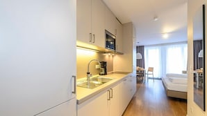 Una habitación de hotel moderna con kitchenette, una cama y zona de estar con vista a la ciudad.