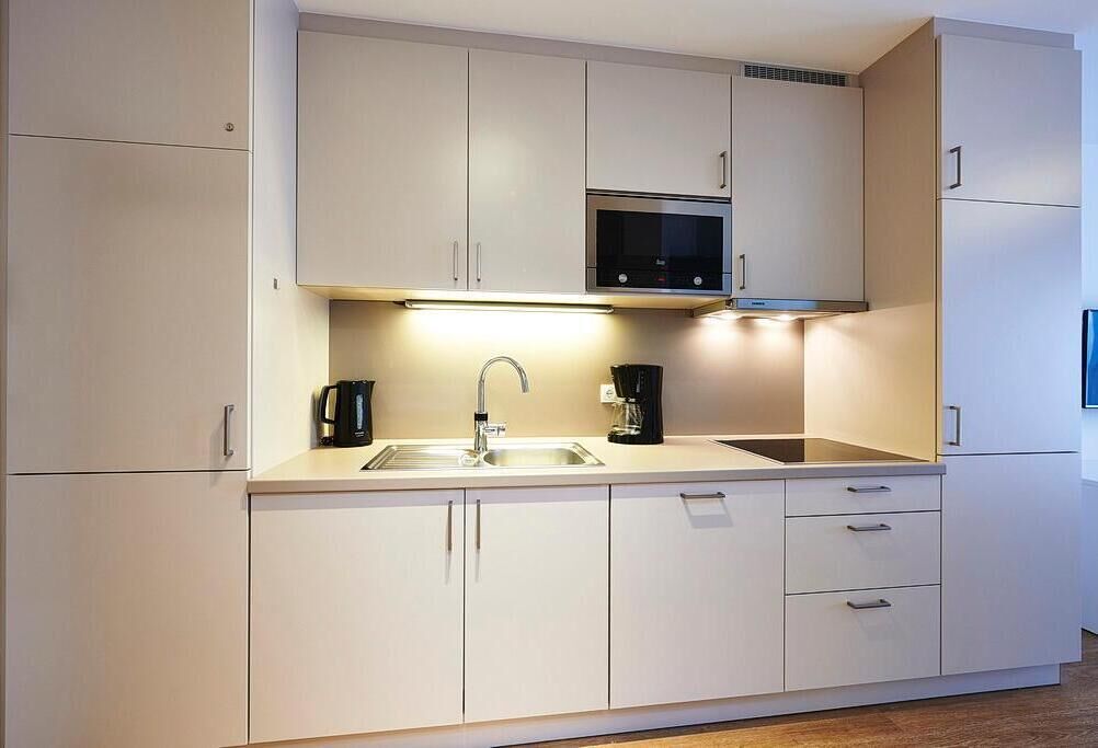 A modern kitchen with white cabinets, a stainless steel microwave, and a coffee maker.