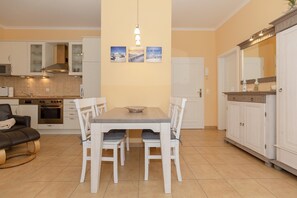Une cuisine moderne avec des meubles blancs, une table à manger entourée de quatre chaises et un luminaire suspendu.