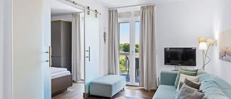 Una sala moderna con un conjunto de sofás, un televisor de pantalla plana y un puertas corredera que dan a un balcón.