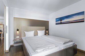 A modern hotel room with a large bed, a nightstand, a desk, and a painting of a sunset.