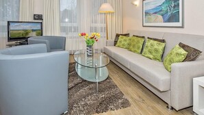 Un salon moderne avec un canapé, une table basse en verre, un téléviseur et un tableau accroché au mur.