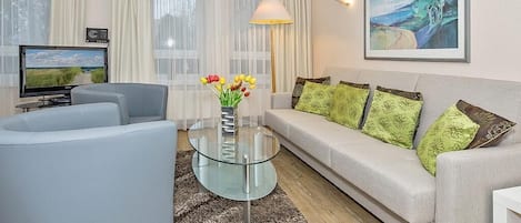 Una sala de estar moderna con un sofá, una mesa de centro de vidrio, un televisor y un cuadro en la pared.