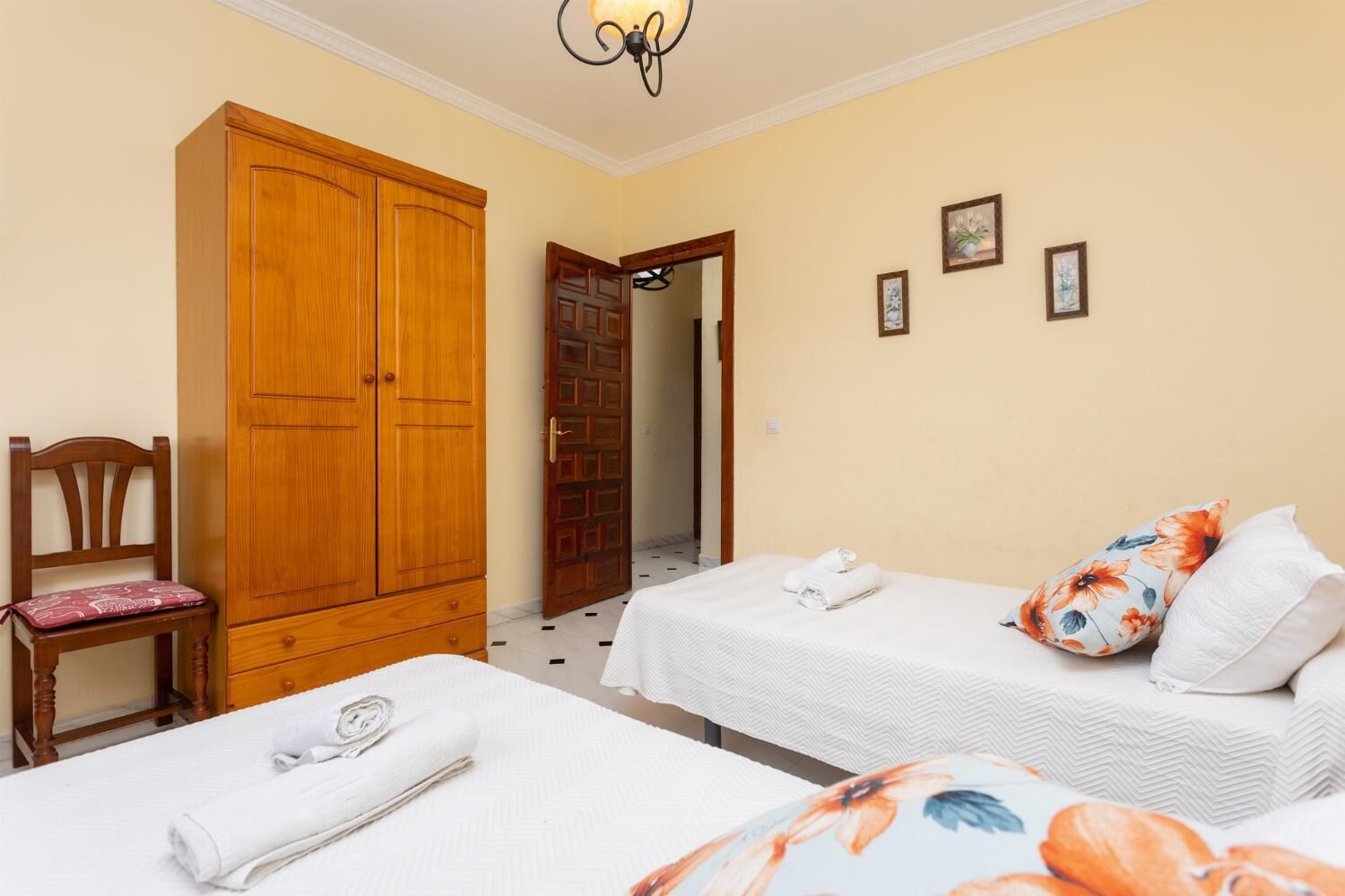Un dormitorio con dos camas, un armario de madera, una silla y una puerta que da a otra habitación.