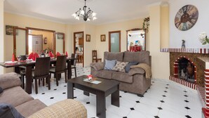 A living room with a sofa, coffee table, and dining area with chairs and a table set for a meal. - Villa Las Palomas - Three Bedroom Villa, Sleeps 6 (Frigiliana)