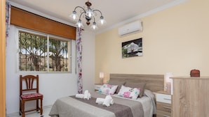 A bedroom with a bed, a chair, a nightstand, a dresser, a window with a view of trees, and a ceiling light fixture. - Villa Las Palomas - Three Bedroom Villa, Sleeps 6 (Frigiliana)
