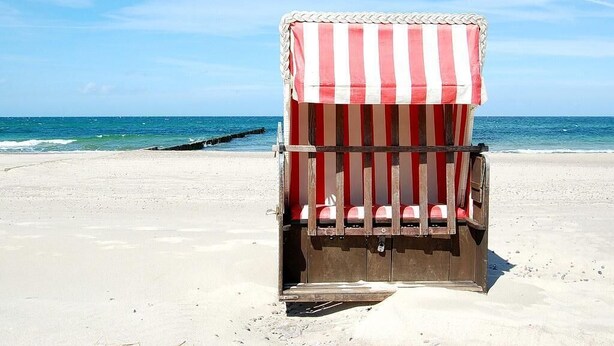 Ein Liegestuhl mit einem gestreiften Sonnendach, platziert an einem sandigen Strand mit dem Meer im Hintergrund.