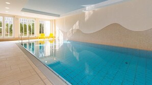 Ein Innenpool mit klarem, blauem Wasser, Fliesenboden und einem wellenförmigen Wanddesign.