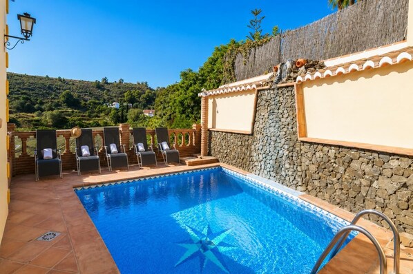 A swimming pool with a star-shaped design, surrounded by lounge chairs and a stone wall.
