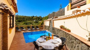 A poolside dining area with a table set for two, surrounded by lounge chairs, and a view of a hillside. - Villa Las Palomas 2 - Three Bedroom Villa, Sleeps 5 (Frigiliana)