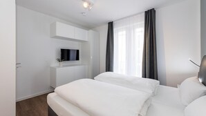 Une chambre d’hôtel avec un lit, un téléviseur fixé à un meuble blanc et une fenêtre avec des rideaux.