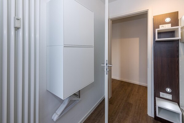 A hallway with a white wardrobe, a wooden door, and a small white shelf unit with a power outlet.