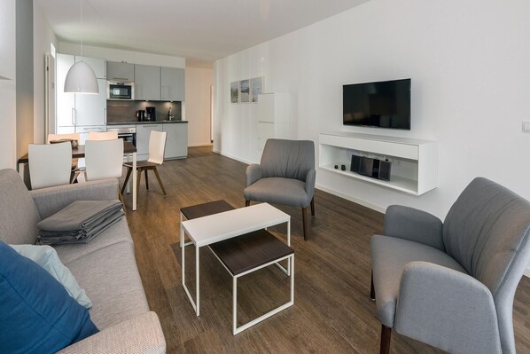 Una sala de estar moderna con sofás grises, una mesa de centro y un televisor montado en la pared.