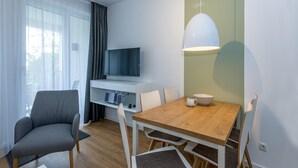 Un salon moderne avec un téléviseur à écran plat, une table à manger avec quatre chaises, un canapé gris et une table basse blanche.
