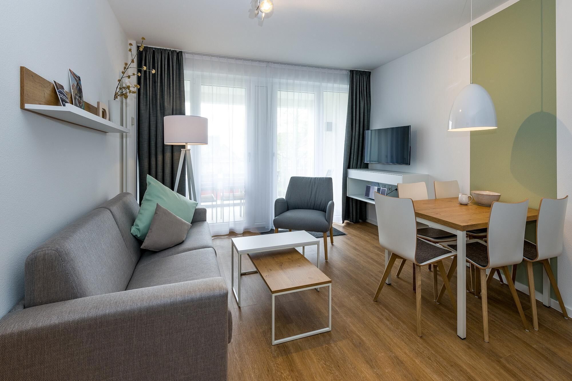 A modern living room with a sofa, a dining table with chairs, a TV, and a lamp.