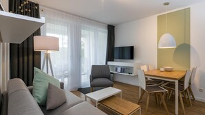 Un salon moderne comprenant un canapé, une table basse, une table à manger avec des chaises, un téléviseur fixé au mur et une lampe.