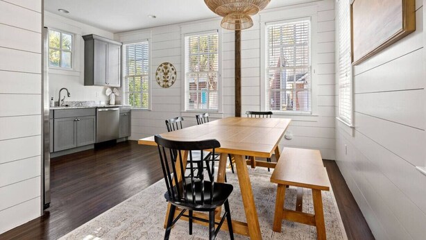 A modern kitchen with white cabinetry, a wooden dining table, and a large window with blinds. - Historic Charleston Single w/ Private Outdoor Space (Charleston)