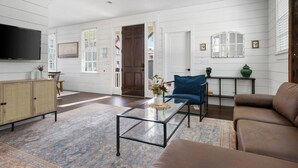 A spacious living room with a large flat-screen TV, a glass coffee table, a brown sofa, and a blue armchair. - Historic Charleston Single w/ Private Outdoor Space (Charleston)