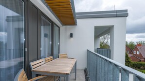 Ein Balkon mit Holztisch und -stühlen, einer Glastür und einer weißen Wand mit einem Fenster.