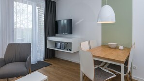 Ein modernes Wohnzimmer mit Flachbildfernseher, Esstisch mit Stühlen, einer Couch und einer Pendelleuchte.