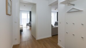 Eine moderne Wohnung mit Holzboden, weißen Wänden und einem Flur, der in einen Wohnbereich mit einer Couch und einem Sessel führt.