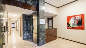 A hotel lobby with a marble reception desk, a glass door entrance, and a corridor leading to other rooms.