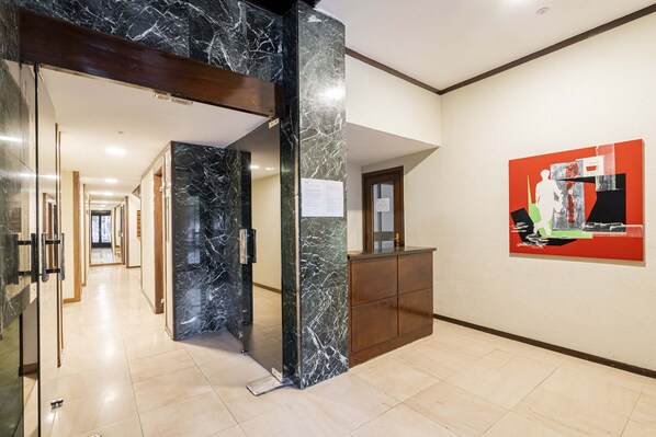 Un hall d’hôtel avec un comptoir de réception en marbre, une entrée avec une porte en verre et un couloir menant aux autres chambres.
