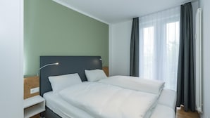 Une chambre d’hôtel moderne avec un grand lit, une table de chevet, une commode et une fenêtre avec des rideaux.