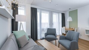 Un salon moderne avec un canapé gris, deux fauteuils, une table basse en bois et un coin repas comprenant une table et des chaises.