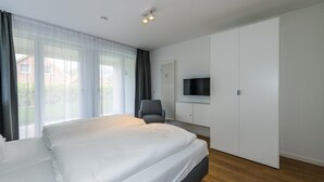 A modern bedroom with a large bed, a grey armchair, a TV mounted on the wall, and a radiator.