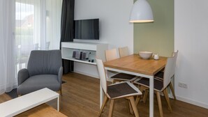 A modern living room with a wooden dining table, grey sofa, and a TV mounted on the wall.