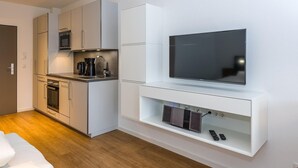 Une cuisine moderne dotée d’appareils électroménagers intégrés, d’un téléviseur à écran plat et d’un petit meuble de divertissement avec télécommandes.