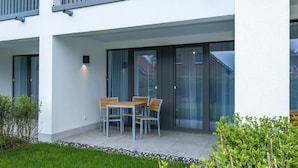 Un bâtiment moderne doté d’un patio comprenant une table et des chaises, de grandes portes-fenêtres coulissantes et une pelouse bien entretenue.