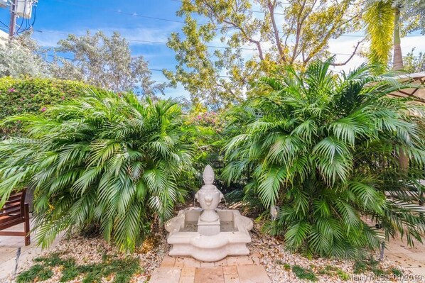 A garden with a central fountain surrounded by lush greenery and palm trees.