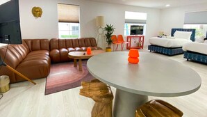 A modern living room with a brown leather sofa, a round coffee table, and a dining table with orange stools.