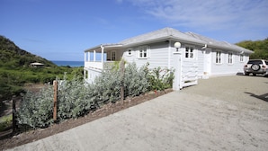 A white two-story house with a balcony, a gravel driveway, and a parked SUV. - Calabash 4 Bedroom Villa - Stunning Sea Views, Private Pool, Delightful Location (Darkwood Valley)