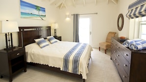 A bedroom with a bed, nightstands, a dresser, a chair, a ceiling fan, a painting, and a window with curtains. - Calabash 4 Bedroom Villa - Stunning Sea Views, Private Pool, Delightful Location (Darkwood Valley)