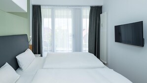 Habitación de hotel con una cama grande, un televisor de pantalla plana montado en la pared y vistas al exterior a través de cortinas traslúcidas.
