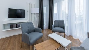 A modern living room with two grey armchairs, a white coffee table, a flat-screen TV, and a white radiator. - Strandnahes Ferienapartment mit Balkon, Parkplatz, Schwimmbad- & Saunanutzung (Nordseeheilbad Bensersiel)