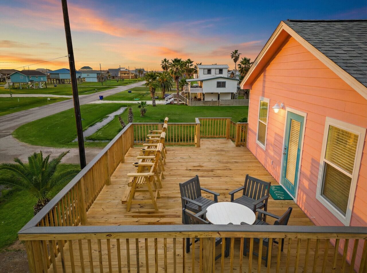 A wooden deck with outdoor seating and a view of a residential area during sunset.