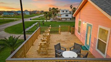 A wooden deck with outdoor seating and a view of a residential area during sunset.