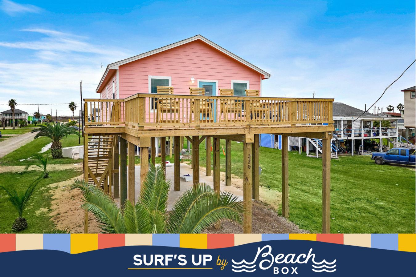 A pink house with a wooden deck and a staircase leading to a second floor.