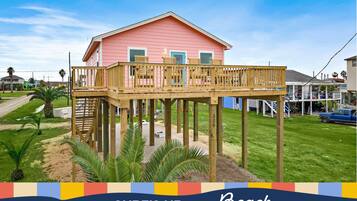 A pink house with a wooden deck and a staircase leading to a second floor.