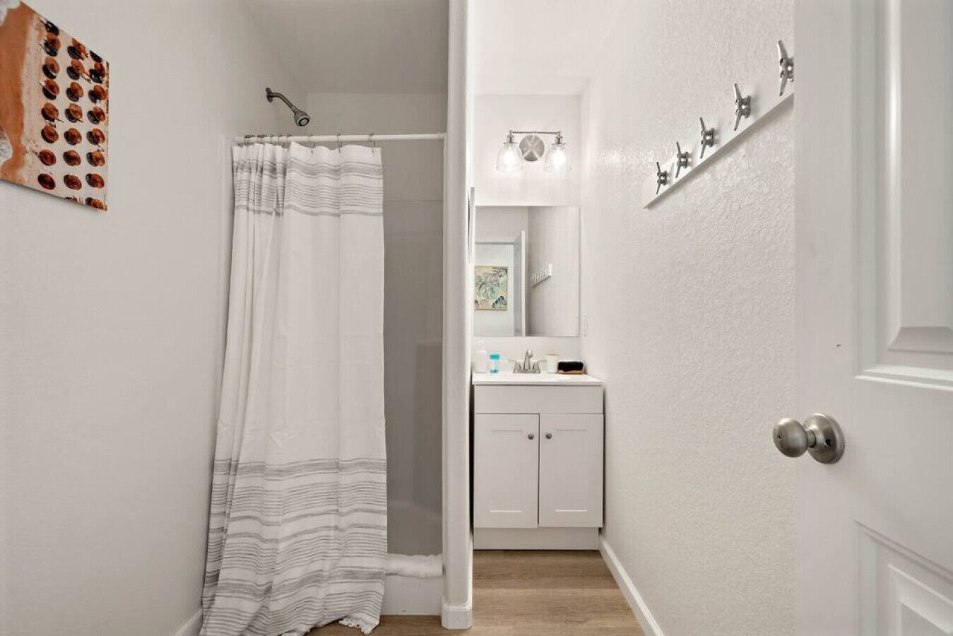 A narrow hallway leading to a bathroom with a shower curtain, a sink, and a mirror.