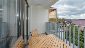 A balcony with a wooden table and chairs, a glass door, and a view of neighboring houses.