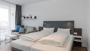 A modern hotel room with a large bed, a sofa, a small table, and a bedside lamp.