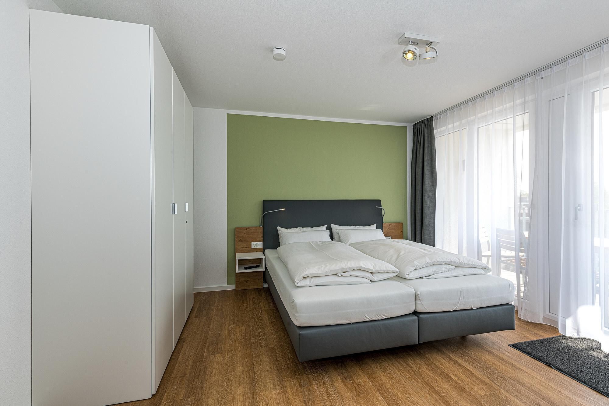 Une chambre à coucher comprenant un lit, une table de chevet, une armoire et une fenêtre avec des rideaux.