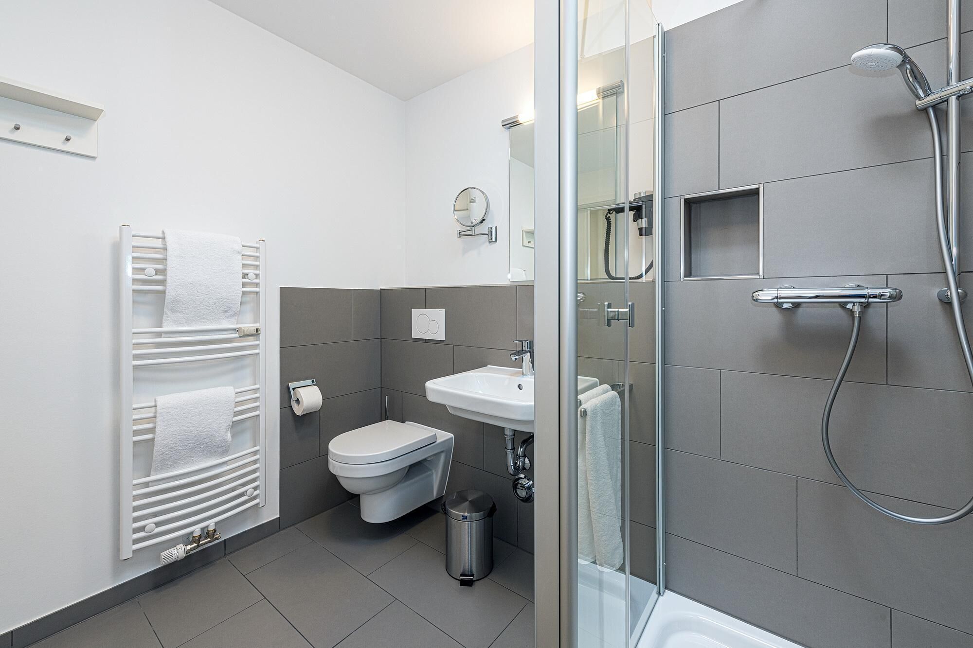 Un baño moderno con cabina de ducha de vidrio, inodoro blanco, lavamanos y toallero.